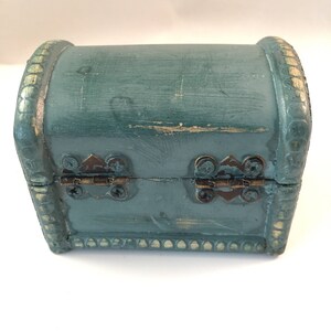 May include: A small teal blue wooden treasure chest with gold accents and brass hinges. The chest is closed.