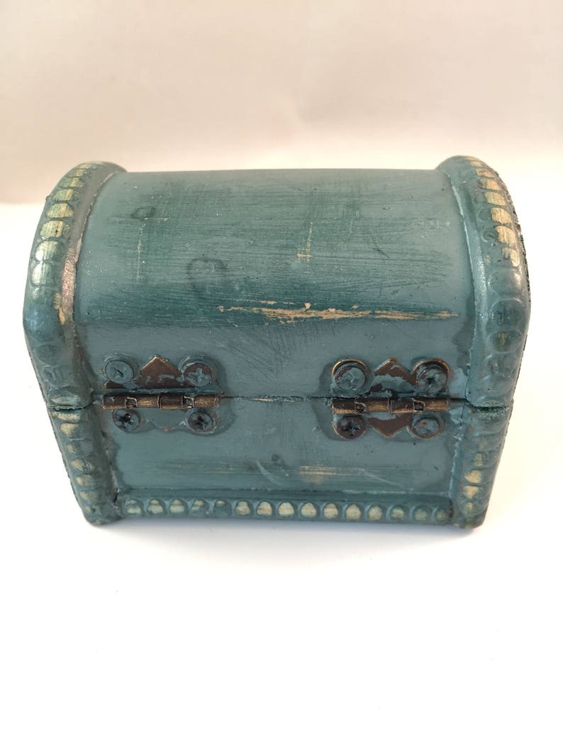 May include: A small teal blue wooden treasure chest with gold accents and brass hinges. The chest is closed.