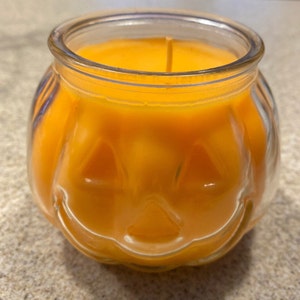 Pode incluir: Um porta-velas de vidro em forma de ab&oacute;bora com uma vela laranja brilhante dentro. A vela est&aacute; acesa e a chama &eacute; vis&iacute;vel.