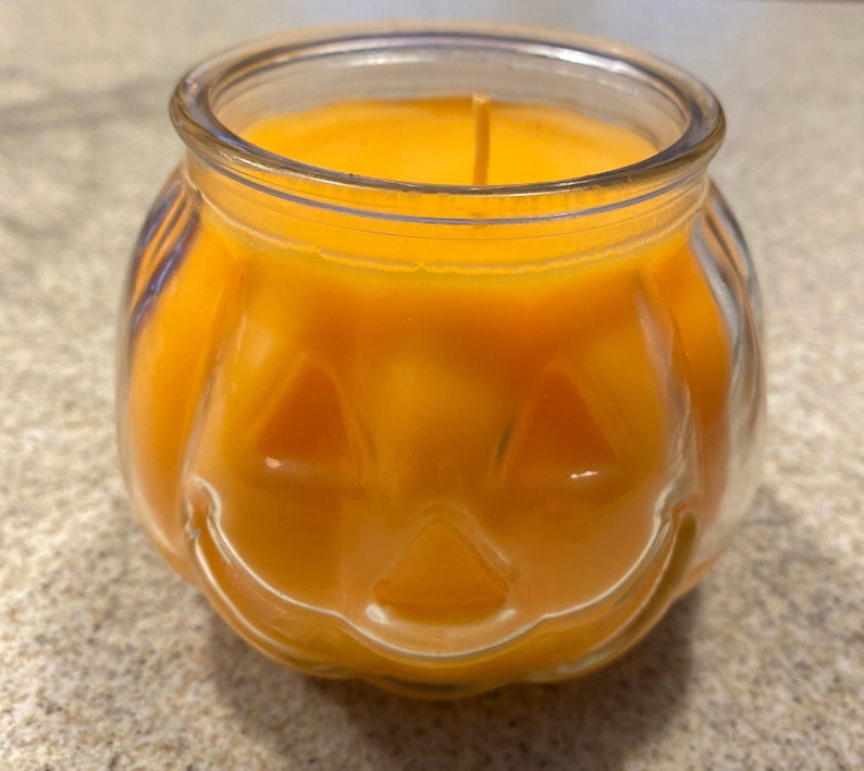 Pode incluir: Um porta-velas de vidro em forma de ab&oacute;bora com uma vela laranja brilhante dentro. A vela est&aacute; acesa e a chama &eacute; vis&iacute;vel.