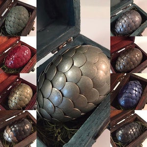 May include: A set of six dragon eggs, each with a different metallic finish, in a wooden box. The eggs are made of metal and have a scaly texture. The colors include silver, gold, red, green, blue, and black.