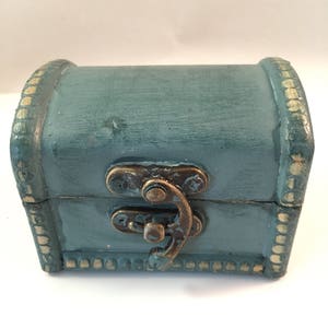 May include: A small, teal blue wooden treasure chest with a brass latch and gold trim. The chest is closed.