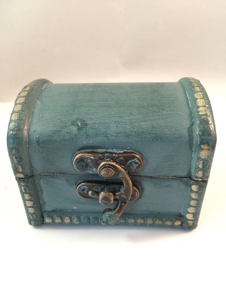 May include: A small, teal blue wooden treasure chest with a brass latch and gold trim. The chest is closed.