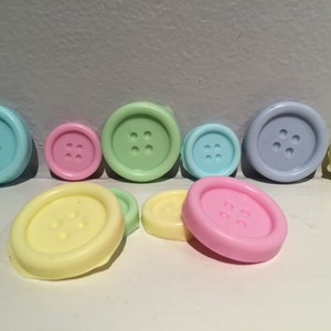May include: Assortment of pastel colored buttons with four holes each. The buttons are in shades of blue, green, pink, and yellow.