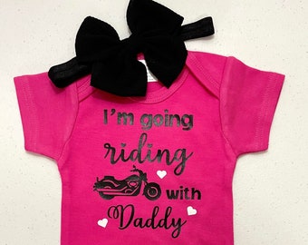 Könnte beinhalten: Rosaer Baby-Strampler mit schwarzem Text, der "Ich fahre mit Papa Motorrad" lautet, und einer schwarzen Motorradgrafik. Der Strampler hat ein schwarzes Stirnband mit Schleife.
