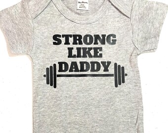 May include: Gray baby onesie with black text that reads "Strong Like Daddy" with a barbell graphic.