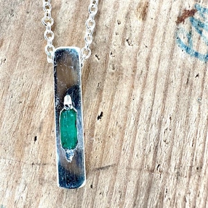 Op de afbeelding: Zilveren hangerketting met een rechthoekige hanger. De hanger bevat een heldergroene edelsteen. De ketting is een fijne zilveren schakelketting. Een eenvoudig en elegant ontwerp voor elke gelegenheid.
