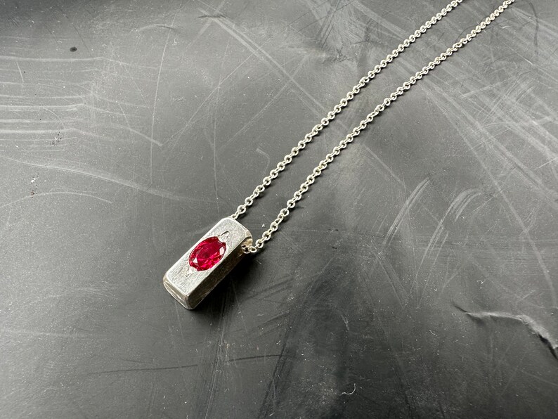 a silver necklace with a red stone on it