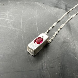 a silver necklace with a red stone on it