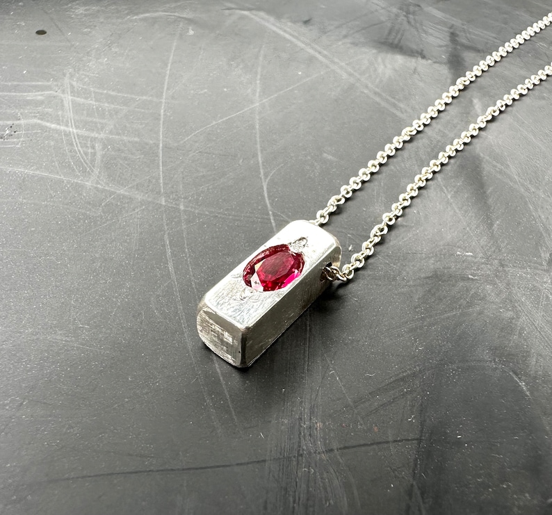 a silver necklace with a red stone on it