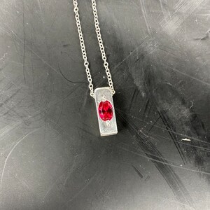 a silver necklace with a red stone on it