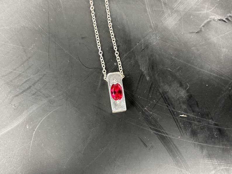 a silver necklace with a red stone on it