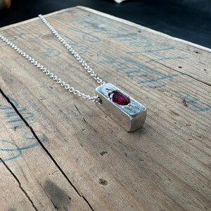 a necklace with a red stone sitting on top of a wooden table