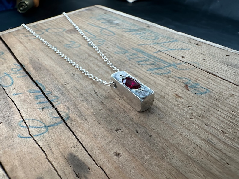 a necklace with a red stone sitting on top of a wooden table