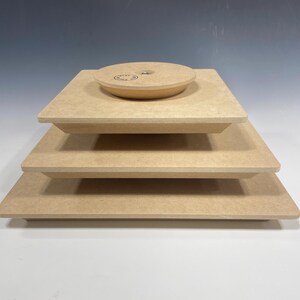 May include: Four stacked square wooden platforms, the top platform has a round wooden base with a small screw in the center.