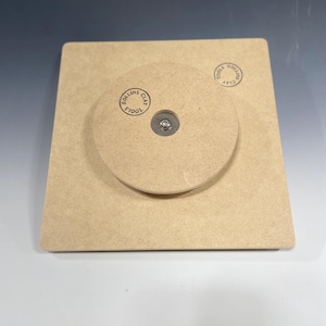 May include: A square wooden base with a round wooden disc on top. The disc has a metal screw in the center and a circular stamp that reads "TOOLS CLAY ROLLINS".