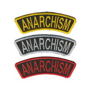 May include: Three embroidered patches displaying the word "ANARCHISM" in a curved banner design. The patches are in yellow, silver, and red, each with a black background and contrasting thread colours. These patches are likely for clothing or accessories.