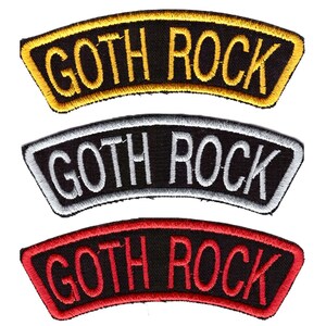 Puede incluir: Tres parches bordados con la inscripción "GOTH ROCK". El parche superior tiene letras y ribetes dorados sobre fondo negro. El parche central tiene letras y ribetes blancos sobre fondo negro. El parche inferior tiene letras y ribetes rojos sobre fondo negro.