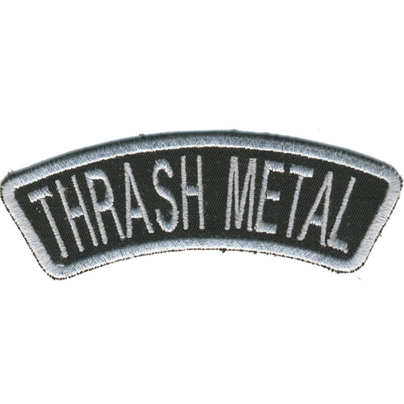 May include: A black, arched patch with the words "THRASH METAL" embroidered in white. The patch has a silver border and is likely designed to be sewn onto clothing or accessories.
