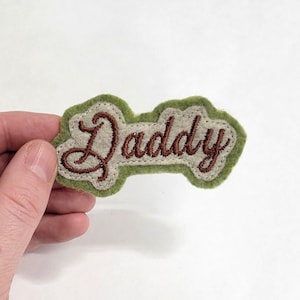 May include: Green felt patch with the word "Daddy" embroidered in brown thread.