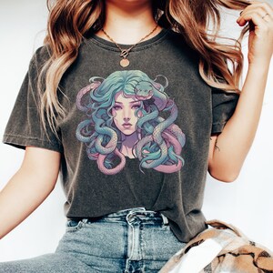 Pode incluir: Uma camiseta cinza escura com uma estampa gr&aacute;fica de uma mulher com cobras azuis e roxas no cabelo.