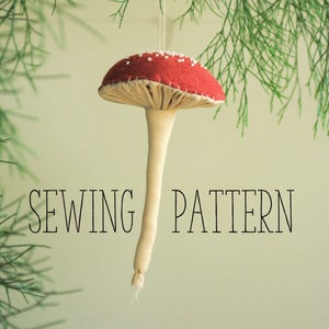 May include: A red and white felt mushroom ornament with a white stem and the text "SEWING PATTERN" on a green background.