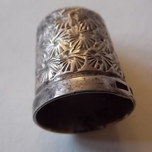 Puede incluir: Dedal de plata con un dise&ntilde;o floral. El dedal est&aacute; hecho de metal y tiene un acabado liso y brillante.