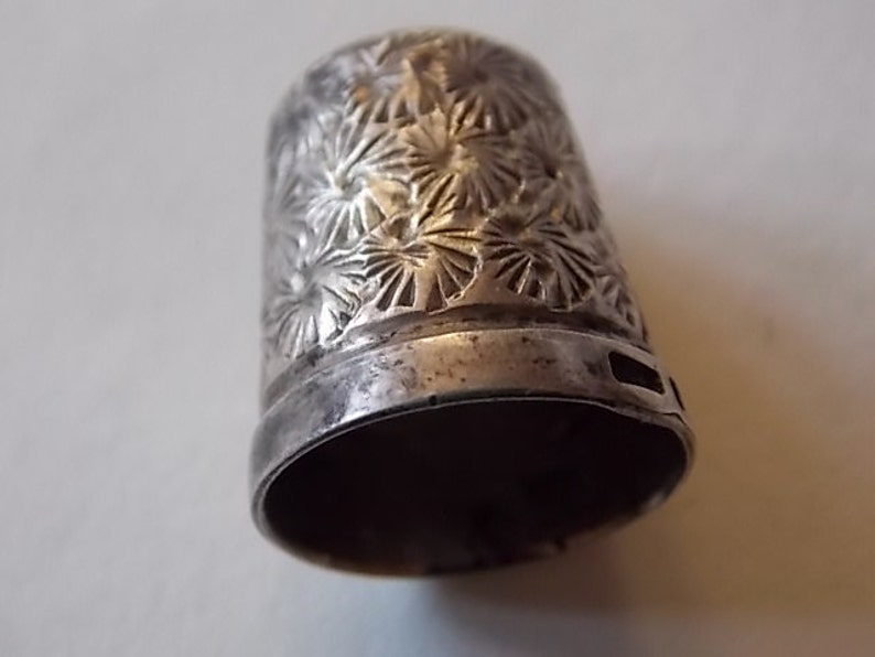 Puede incluir: Dedal de plata con un dise&ntilde;o floral. El dedal est&aacute; hecho de metal y tiene un acabado liso y brillante.