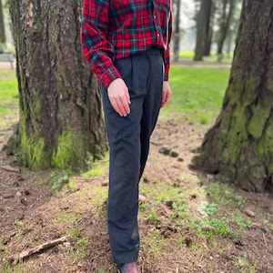 May include: A person wearing a red and green plaid flannel shirt over a black and white striped shirt, paired with dark gray trousers and brown leather boots. The outfit is casual and suitable for outdoor activities.