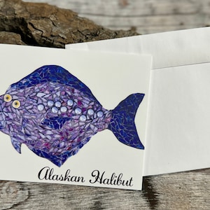 May include: A greeting card featuring a mosaic illustration of an Alaskan Halibut fish with purple and blue tones. The card has the text "Alaskan Halibut" printed below the fish.