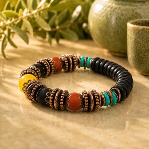 May include: A beaded bracelet featuring black, yellow, orange, and turquoise beads. The bracelet has copper-colored metal accents. The beads are strung together to form a circular shape. The bracelet is a piece of jewelry.