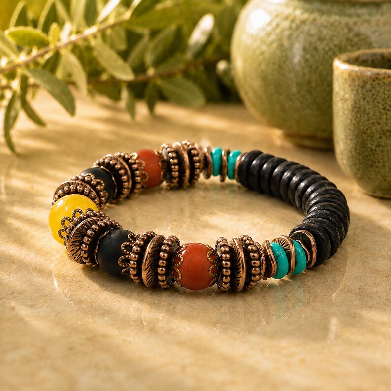 May include: A beaded bracelet featuring black, yellow, orange, and turquoise beads. The bracelet has copper-colored metal accents. The beads are strung together to form a circular shape. The bracelet is a piece of jewelry.