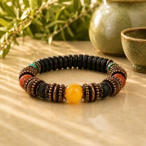 May include: A beaded bracelet featuring a central yellow stone, flanked by black, orange, and turquoise beads. The bracelet has copper-colored accents and a dark wooden bead base. A unique piece of jewelry.