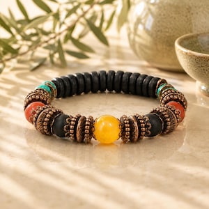 May include: A beaded bracelet featuring a central row of black wooden beads. The bracelet incorporates orange, turquoise, and yellow beads, along with decorative copper-colored metal accents. The bracelet is designed for everyday wear.