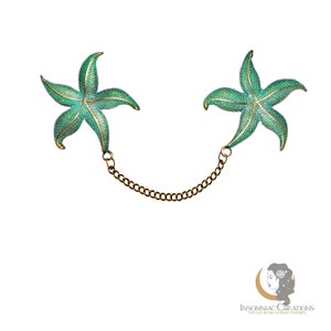 May include: A pair of green enamel starfish brooches connected by a gold chain. The brooches are detailed with a textured finish and gold accents.