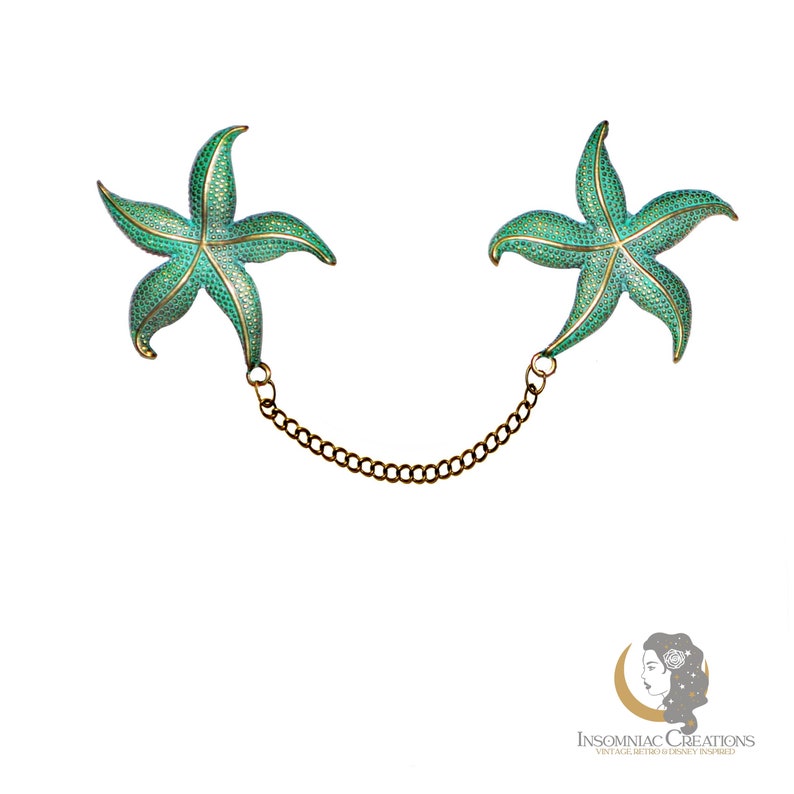 May include: A pair of green enamel starfish brooches connected by a gold chain. The brooches are detailed with a textured finish and gold accents.
