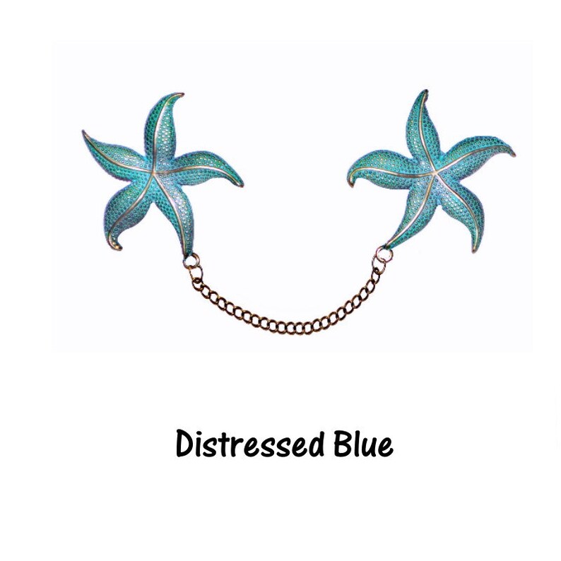 May include: A pair of blue starfish-shaped brooches connected by a chain. The brooches have a distressed blue finish.