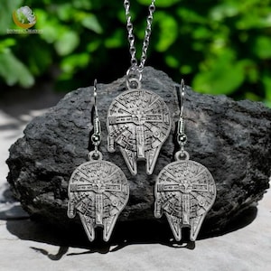 May include: A silver necklace and earrings set featuring a detailed design of the Millennium Falcon spaceship from Star Wars.