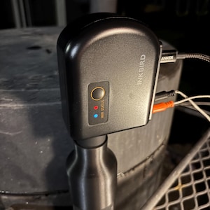 以下が含まれることがあります： 黒いInkbird Wi-Fiステータスデバイス。丸いボタンと「Wi-Fi Status」の文字があります。デバイスには赤と青のライトがあります。Ankerケーブルと他のケーブルがデバイスに接続されています。