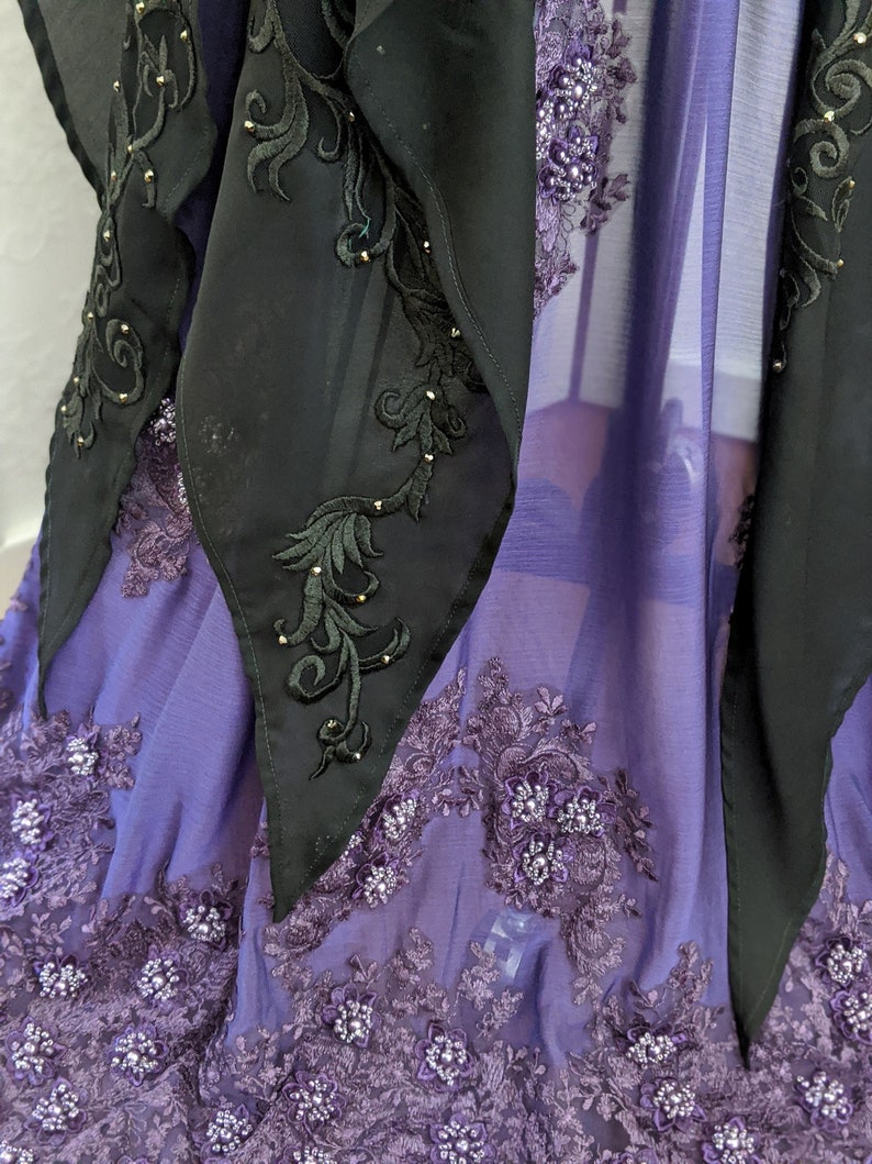 May include: A purple sheer fabric with black lace trim and black embroidered details. The fabric is decorated with small, shiny beads.