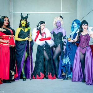 May include: Seven women dressed as Disney villains. They are wearing elaborate costumes and accessories, including a red dress, a green dress, a black dress, a purple dress, a blue dress, a black dress with a white fur collar, and a purple dress with a red cape.