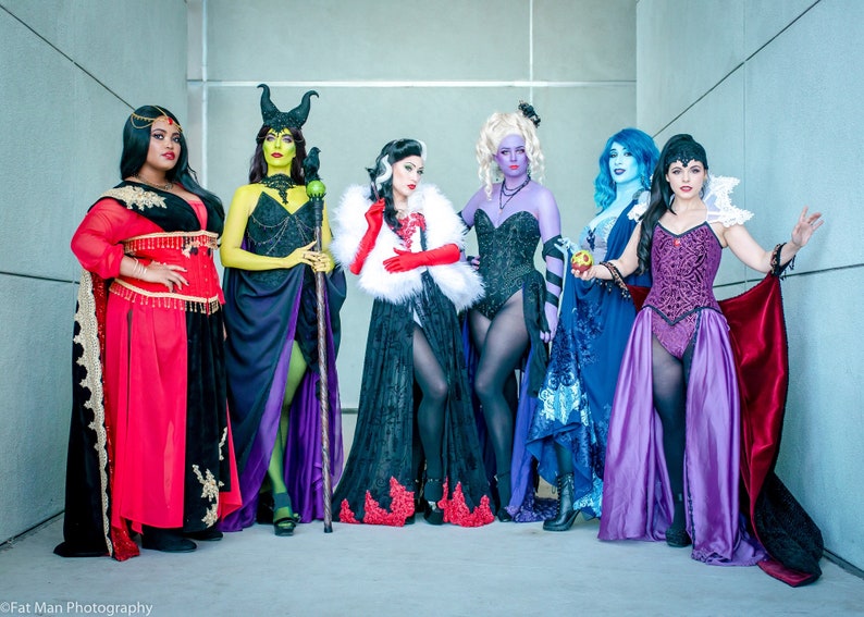 May include: Seven women dressed as Disney villains. They are wearing elaborate costumes and accessories, including a red dress, a green dress, a black dress, a purple dress, a blue dress, a black dress with a white fur collar, and a purple dress with a red cape.