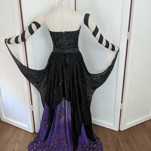 May include: A black and purple formal gown with a high-low hemline. The gown features a strapless bodice with black beading and a purple tulle overlay. The gown is accented with black and white striped sleeves.