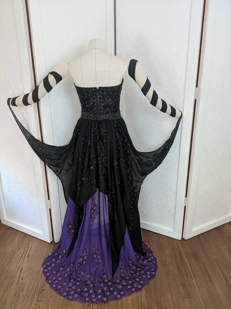 May include: A black and purple formal gown with a high-low hemline. The gown features a strapless bodice with black beading and a purple tulle overlay. The gown is accented with black and white striped sleeves.