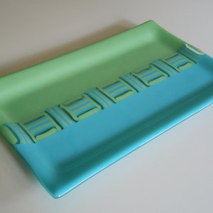 May include: A rectangular glass serving tray with a light green top and a turquoise bottom. A geometric pattern in shades of green and blue is visible on the tray.