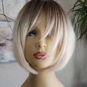 Może przedstawiać: Krótka, prosta, blond peruka z przedziałkiem z boku i grzywką. Peruka jest stylizowana subtelnym efektem ombre, przechodzącym od ciemniejszego blondu u nasady do jaśniejszego blondu na końcach.