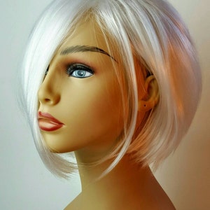 Może przedstawiać: Biała peruka typu bob z przedziałkiem z boku. Peruka jest ułożona w lekkie fale i jest noszona na głowie manekina.