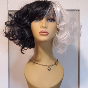 Puede incluir: Una peluca negra y blanca con raya lateral. La peluca está peinada con rizos sueltos. La peluca está en una cabeza de maniquí.