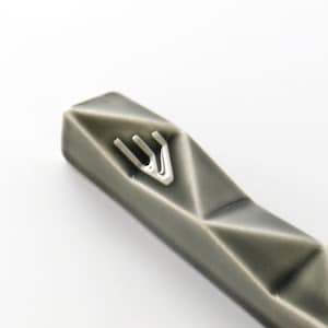 May include: A grey ceramic mezuzah with a silver Star of David on the front. The mezuzah is shaped like a long, thin rectangle with a pointed end.