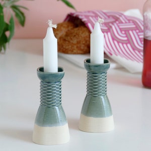 Peut inclure: Deux bougeoirs en céramique avec un design rayé vert et blanc. Les bougeoirs sont sur une surface blanche.